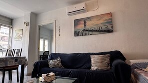 A living room with a dark blue sofa, a glass coffee table, and a painting of a lighthouse on the wall. - Apartment 'Apartamento Martinez Maldonado' with Wi-Fi and Air Conditioning (Málaga)