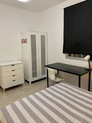 A bedroom with a bed, a desk, a wardrobe, and a window with a black blind.