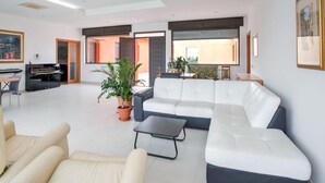 Een ruime woonkamer met een modulaire bank, een piano en een eethoek.
