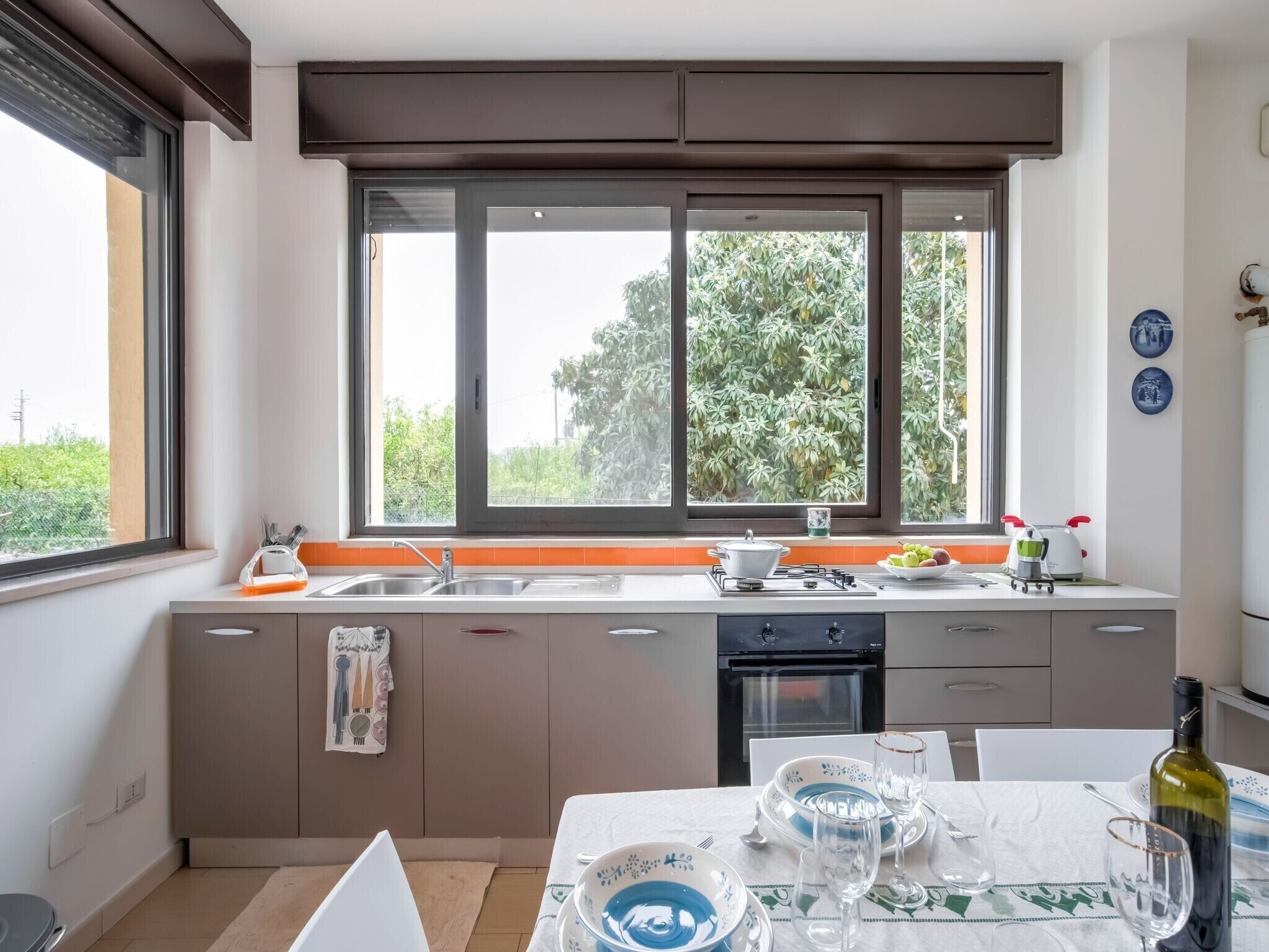 Een moderne keuken met een groot raam, een fornuis en een eettafel gedekt voor twee personen.