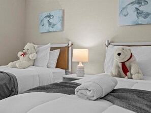 A hotel room with two beds, white bedding, a nightstand with a lamp, and two white teddy bears.