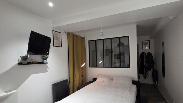 A modern hotel room with a bed, a flat-screen TV mounted on the wall, a desk with a chair, and a wardrobe.
