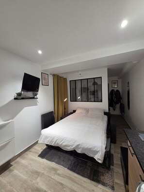 Een moderne hotelkamer met een bed, een flatscreen televisie aan de muur, een bureau met stoel en een kledingkast.