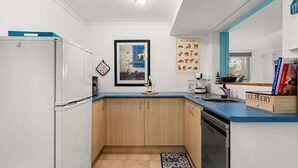 Eine kompakte Küche mit Kühlschrank, Backofen und Geschirrspüler. Über der Arbeitsfläche hängt ein gerahmtes Kunstwerk und auf dem Boden liegt ein kleiner Teppich.