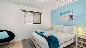 Ein modernes Hotelzimmer mit Bett, Sessel, Nachttisch, Fenster und Wandkunst zum Thema Strand.
