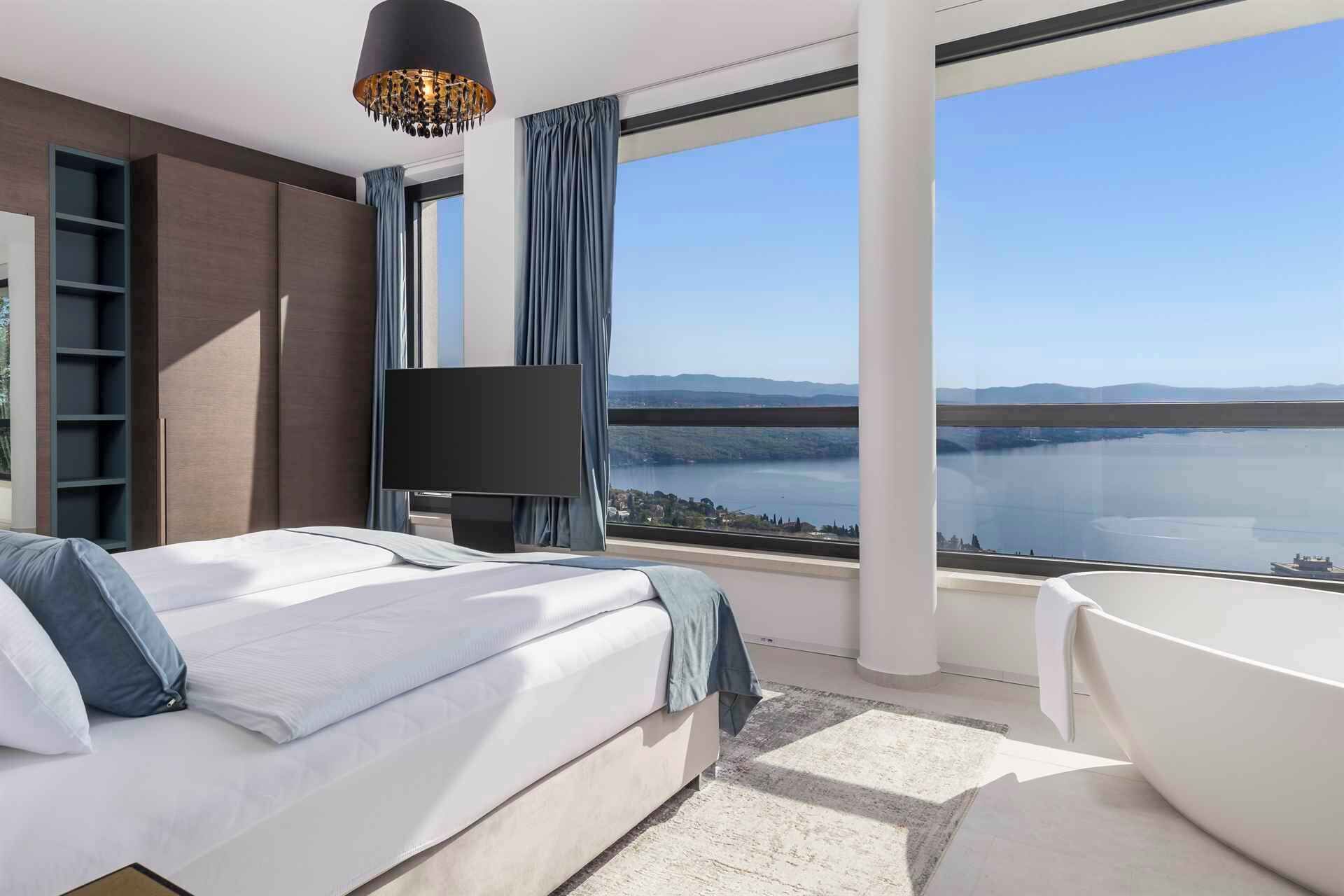 Une chambre d’hôtel moderne dotée d’un grand lit, d’une télévision, d’une baignoire et offrant une vue sur un lac.