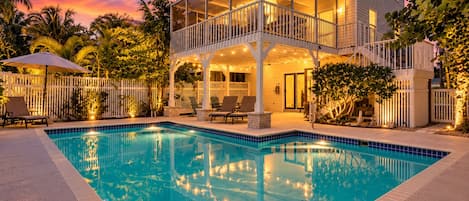 Una casa de dos pisos con piscina, mobiliario exterior y una cerca blanca.