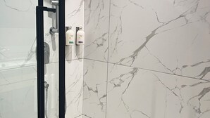 Un baño moderno con cabina de ducha de vidrio, azulejos de mármol y artículos de aseo colgados en la pared.