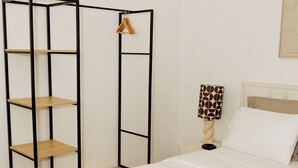 Een netjes opgemaakt hotelkamer met een bed, een houten garderobe en een nachtkastje met een lamp.