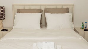 A neatly made bed with white linens, two pillows, and a folded towel with a card on it. There are two bedside tables with a bottle and a glass on one. - Chic & Moderne Studio at Sacré-Cœur 1, Dakar (Dakar)
