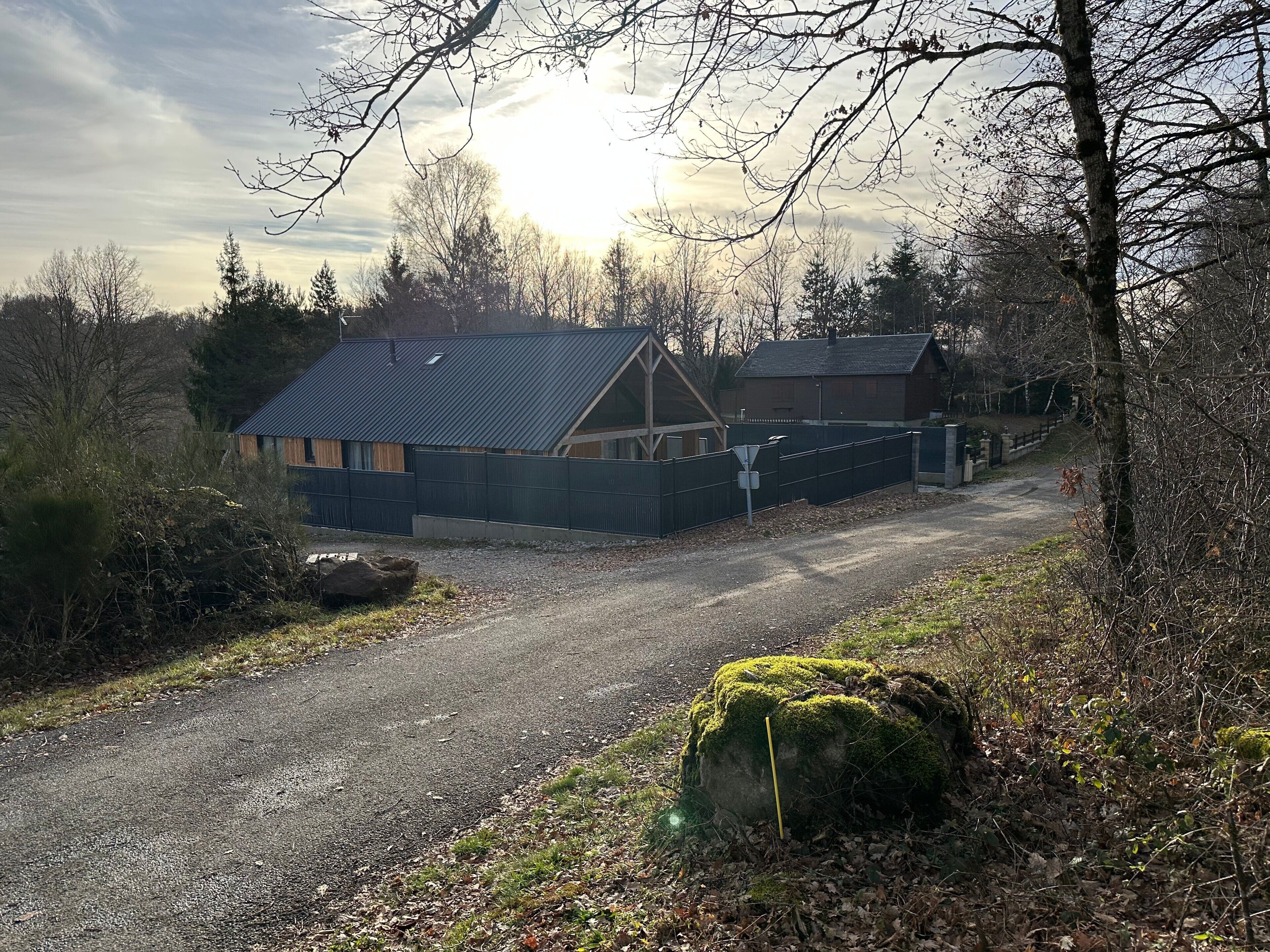 A rural property with a gravel driveway leading to a house with a metal roof and a fenced yard.