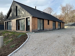 Un bâtiment moderne doté de grandes fenêtres, d’un toit en pente et d’une allée gravillonnée.