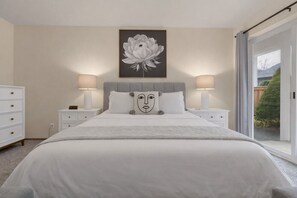 Ein Schlafzimmer mit einem großen Bett, zwei Nachttischen mit Lampen, einer Kommode und einem Wandbild einer Blume.