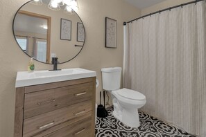 Ein Badezimmer mit einem weißen Waschbecken, einem Holz-Waschtisch, einer Toilette und einer Duschvorhang.