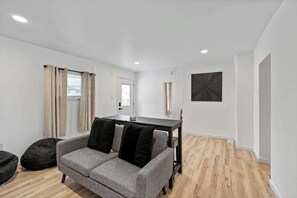 Un salón moderno con un sofá gris, cojines negros, una mesa de centro de madera y un sillón de saco negro.
