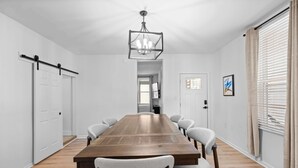 A spacious room with a long wooden table, white chairs, a chandelier, and a large window with blinds. - Rivers Edge Retreat For 10ppl (Dayton)