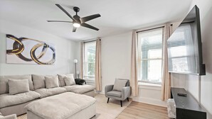 A modern living room with a sectional sofa, a small armchair, a flat-screen TV, and a ceiling fan. - Rivers Edge Retreat For 10ppl (Dayton)