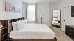 A bedroom with a bed, bedside tables, a ceiling fan, a window with curtains, a lamp, a TV, and a door. - Rivers Edge Retreat For 10ppl (Dayton)