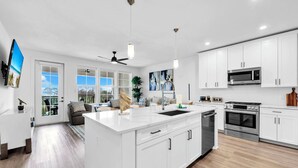 A modern kitchen with white cabinetry, stainless steel appliances, and a large island with a sink. - The Grove Holly 133- 1 Bedroom - Lazy River - Seascape Resort (Miramar Beach)