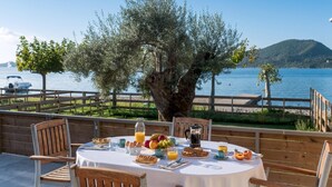 A table set with breakfast items, overlooking a lake with boats and a wooden deck. - Acqua di Mare - Villa Siena (Perigiali)