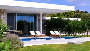 Uma casa moderna com piscina, duas espreguiçadeiras e um espaço de varanda.