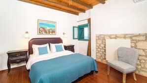 Ein Schlafzimmer mit einem Bett, Nachttischen, einem Sessel, einem Gemälde und einer Steinwand.