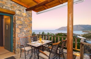 A stone-walled balcony with a table set for two, overlooking a coastal landscape.