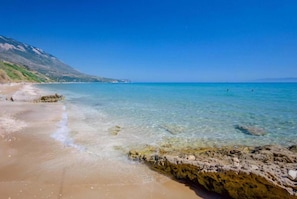A beach with clear water, rocky shoreline, and a distant mountain. - Stylish Villa with Ainos-and-Sea Views set in Mature Gardens near Trapezaki (Kefalonia)