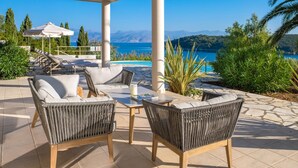 Un espace extérieur aménagé, abrité et doté de mobilier en osier, une piscine et une vue sur la mer et les montagnes.