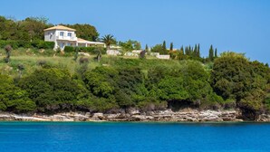 Une propriété située sur la côte, avec une grande maison construite sur une colline, offrant une vue imprenable sur une mer d’un bleu profond.