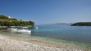 Une plage de galets où sont amarrés des bateaux près du rivage, le tout étant entouré de collines et bordé d’une eau claire.