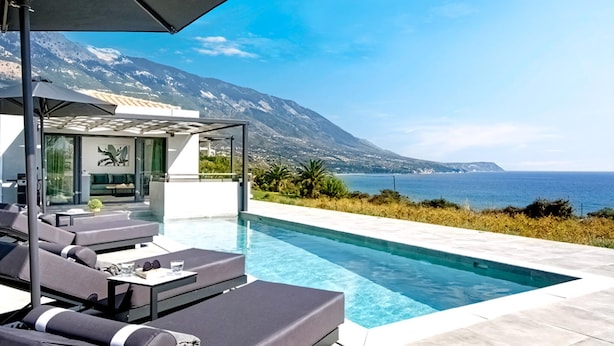 Ein Poolbereich im modernen Stil mit Liegestühlen und einer Pergola, mit Blick auf eine gebirgige Küstenlandschaft.