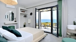 Ein modernes Schlafzimmer mit Bett, einem großen Spiegel, einem Deckenventilator und Meerblick durch eine Schiebetür.