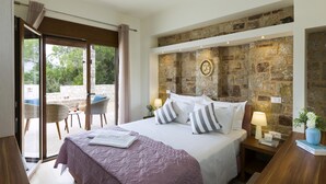Ein Schlafzimmer mit Steingemäuer, einem Bett mit weißer Bettwäsche, gestreifteren Kissen und Blick ins Freie.