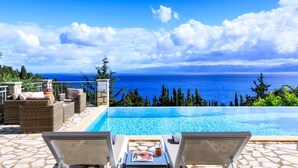 Ein Poolbereich mit Liegestühlen, einer Terrasse mit Steinplatten und Blick auf das Meer.