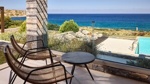 Una terrazza con sedie in vimini e un tavolino che si affaccia su una piscina e il mare.