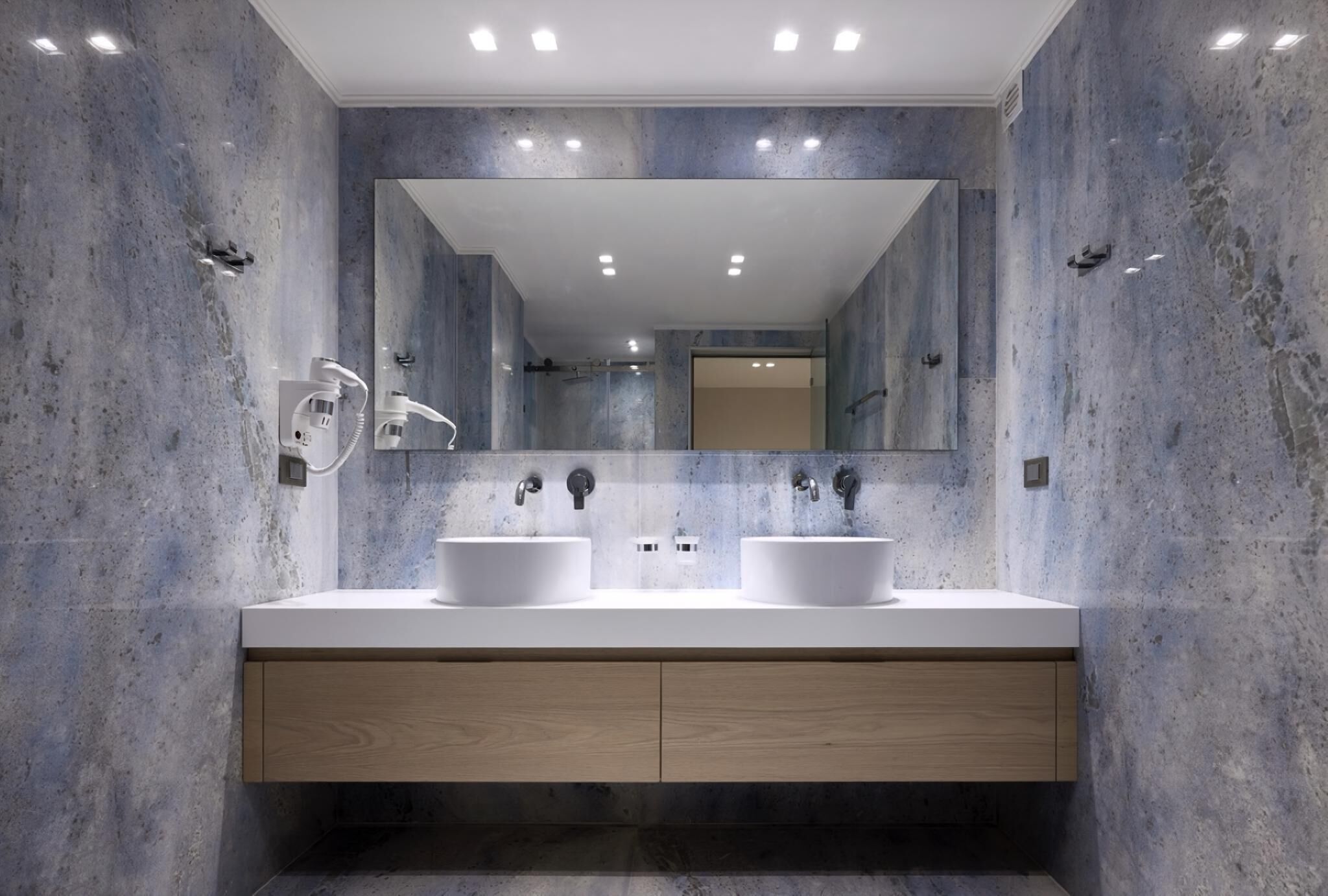 A modern bathroom with two sinks, a large mirror, and recessed ceiling lights.