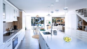 A modern kitchen with white cabinetry, a large island, and pendant lighting. - Stylish Villa with Heated Pool steps from the Beach and Restaurant (Olmeto)
