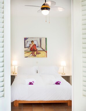 Quarto com cama, duas luminárias de cabeceira, ventilador de teto e um quadro na parede.