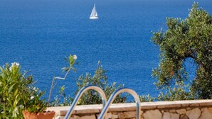 Une piscine avec vue sur la mer et un voilier à l’horizon.