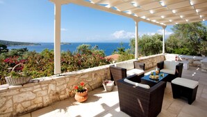 Une terrasse extérieure aménagée avec des meubles en osier, un mur en pierre et une vue sur la mer.