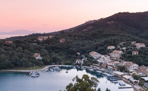 A coastal town with buildings on a hillside, a marina with boats, and a body of water. - Villa Rahi - Charming House with Sea Views in Agios Stephanos near Beach (Sinion)
