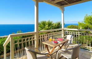 A balcony with wicker chairs, a wooden table, and a view of the sea. - Cosy Villa with Sea-and-Mountain Views near Agios Nikitas (Lefkada)