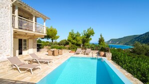 Zona piscina con lettini, un edificio in pietra e vista sul mare.