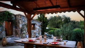 Un espacio para comer al aire libre con un edificio de piedra al fondo, una pérgola de madera y una mesa dispuesta para una comida.