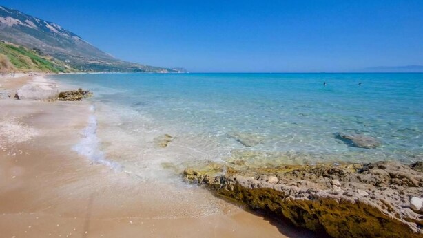 A beach with clear water, rocky shoreline, and a distant mountain. - Stylish Villa with Ainos and Sea Views set in Mature Gardens near Trapezaki (Kefalonia)