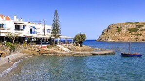 A coastal building with outdoor seating, a rocky shoreline, and a boat. - Mochlos Harbour View (Sitia)