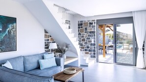 A modern living room with a grey sofa, a wooden coffee table, and a stone wall. - Mochlos Harbour View (Sitia)