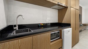 A modern kitchen with wooden cabinets, a black countertop, a stainless steel sink, and a built-in microwave. - Pinjarra Resort (PINJARRA)