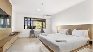 A hotel room with a large bed, a desk, two chairs, a TV, and a window with a view of trees. - Pinjarra Resort (PINJARRA)